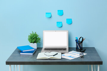 Fototapeta premium Workplace with laptop, charts and notebooks near blue wall