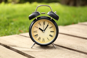 Black vintage alarm clock on bench in park, closeup