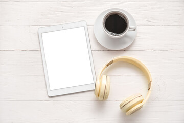 Tablet computer with headphones and coffee cup on white wooden background. Podcast concept