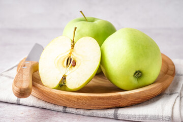 Wooden plate with fresh green apples on light background, closeup