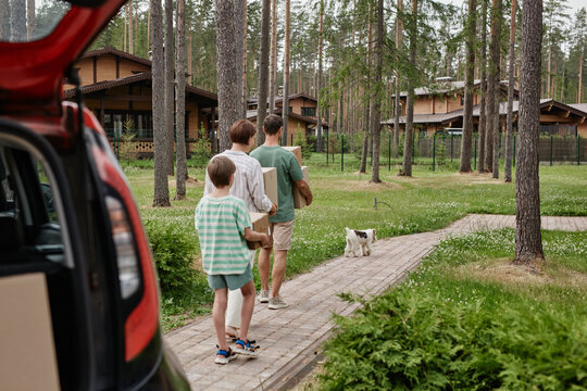 Back View Of Family Unloading Boxes From Car Trunk While Moving Into New House In Nature