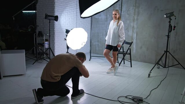 Cameraman working in the modern studio. Man squatted to take a picture of a model’s footwear.
