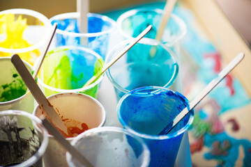 Paint cups in multiple color with mixing sticks, with poured paint in background.   Shallow depth of field.