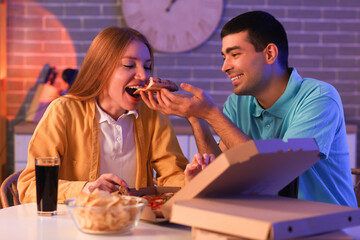Young couple eating tasty pizza in kitchen at night