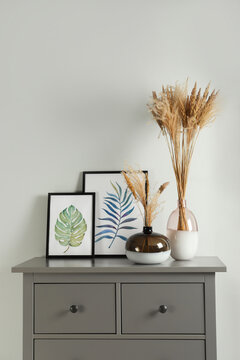 Reed's blossom in glass vases and pictures on grey cabinet indoors