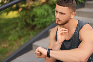 Attractive serious man checking pulse after training on stairs in park. Space for text