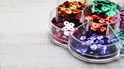 Container with many colorful sequins on white wooden table, closeup. Space for text