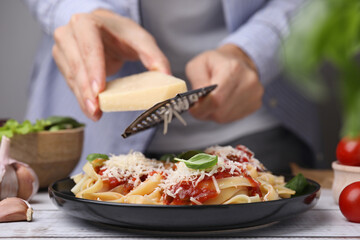 Woman grating parmesan cheese onto delicious pasta at wooden table, closeup