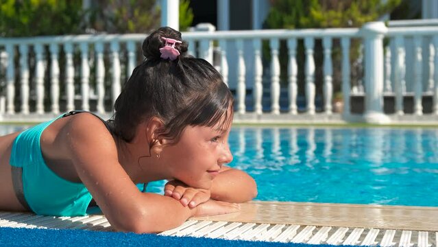 Child bask in the sun by the pool. A little girl sunbathing by the home pool in the day light. A concept of calm summer day by the water.