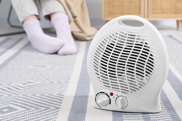 Electric fan heater and woman sitting on chair at home, closeup. Space for text