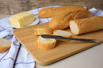 Tasty cut baguette with fresh butter on white table