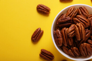 Bowl with tasty nuts on yellow background, flat lay. Space for text