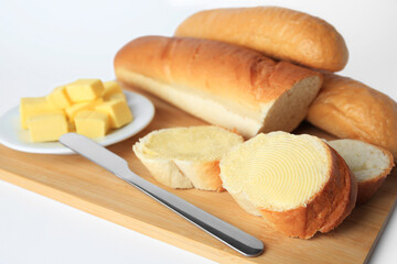 Whole and cut baguettes with fresh butter on white background, closeup