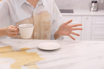 Woman with spilled coffee over her shirt at marble table in kitchen, closeup