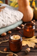 Fototapeta na wymiar Burning scented candles, warm sweaters and acorns on wooden table. Autumn coziness