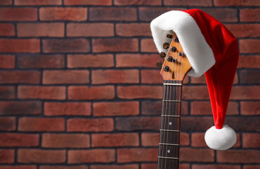 Guitar with cute Santa hat near brick wall, space for text. Christmas music