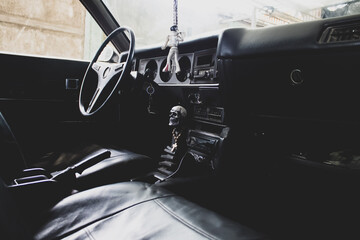 Interior de cuero negro de un vehículo antiguo, volante, palanca de cambios, tablero y adornos