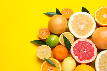 Different ripe citrus fruits with green leaves on yellow background, flat lay. Space for text