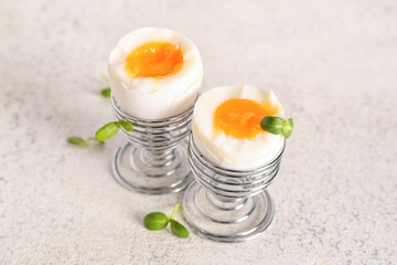 Holders with boiled eggs and leaves on white background