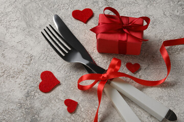 Cutlery for Valentine's Day with red bow, hearts and gift on grunge background, closeup