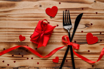 Cutlery for Valentine's Day with bow, hearts and gift on wooden background