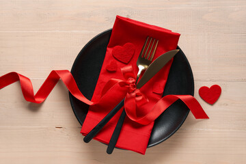Table setting for Valentine's Day with red hearts and bow on wooden background