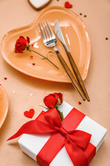 Table setting for Valentine's Day with gift, roses and hearts on beige background, closeup