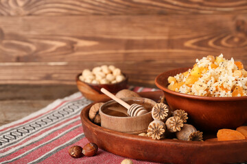 Tray with bowl of rice Kutya, ingredients and poppy pods on napkin near wooden wall