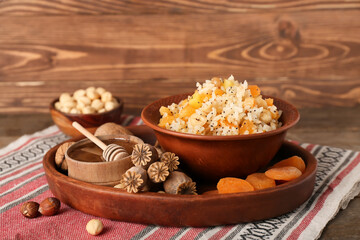 Fototapeta na wymiar Tray with bowl of rice Kutya, ingredients and poppy pods on napkin near wooden wall