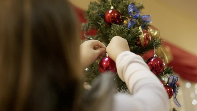 Woman Putting Red Christmas Ball On A Christmas Tree - Decorating Christmas Tree. - low ngle