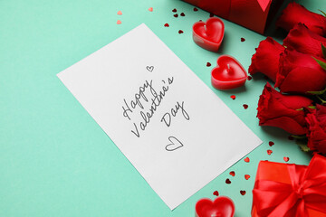 Card with text HAPPY VALENTINE'S DAY, gifts, roses and candles on green background, closeup
