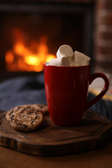 Delicious sweet cocoa with marshmallows, cookies and blurred fireplace on background