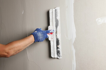 Professional worker plastering wall with putty knife, closeup