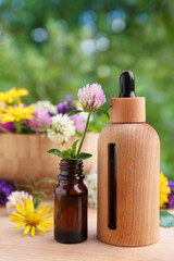 Bottles of essential oil and flowers on wooden table, closeup