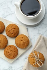 Tasty oatmeal cookies and cup of coffee on white marble table, flat lay