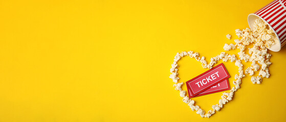 Cinema tickets and heart made of popcorn on yellow background, flat lay with space for text. Banner...