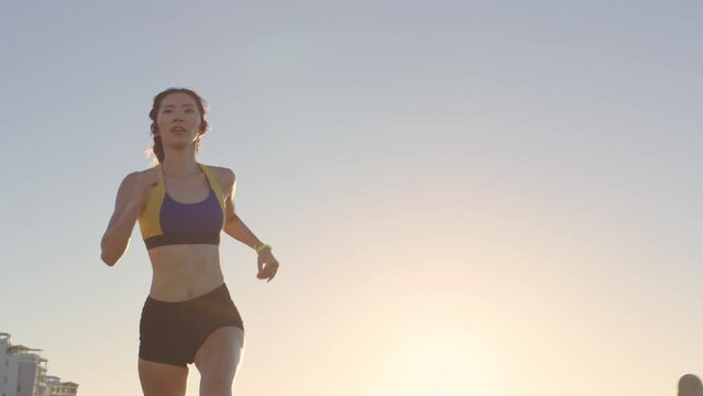 Woman runner, city and sunshine for fitness, health or summer body with music for motivation. Fast running, asian woman athlete or workout for exercise with headphones in metro park, sky and sunshine