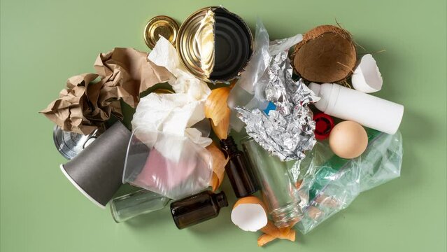 Paper, plastic, organic, metal, paper rubbish appearing one by one on green studio background. Reuse, recycling, ecological safety. Stop motion video, copy space. Endless stop motion video, copy space