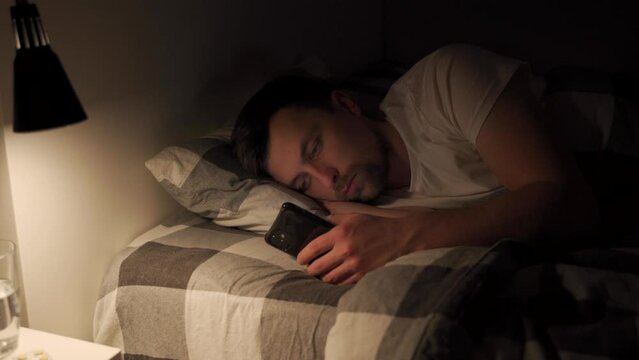 Guy with sore and tired eyes when using gadget at night, sleeplessness, sleep disturbance, blue light screen spoils sleep schedule. Man addicted to internet, social media and chatting on smart phone.
