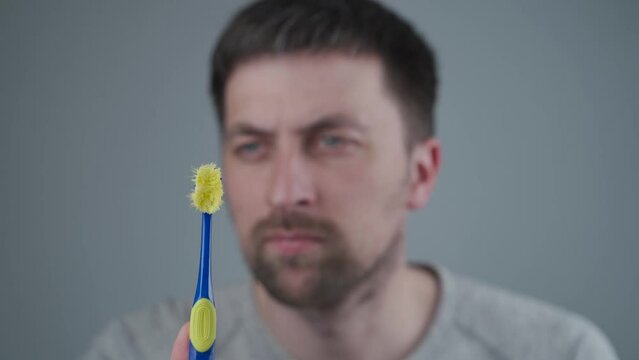 Caucasian man looks disapprovingly at old worn out toothbrush as it is time to buy new one. Importance of replacing toothbrush, oral hygiene. Dental care. My faithful old toothbrush to say goodbye.