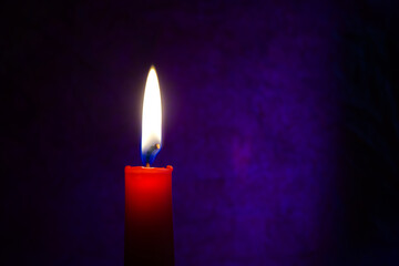 Single red candle burning alone in the dark blue
