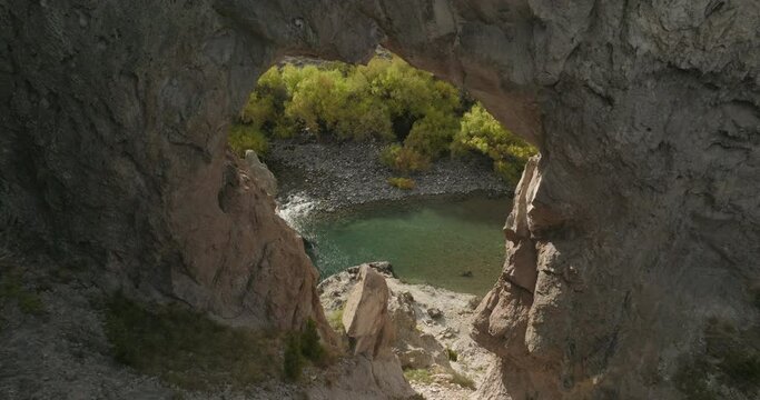 Gorgeous drone shot flying through a rock formation towards a beautiful river in Argentina