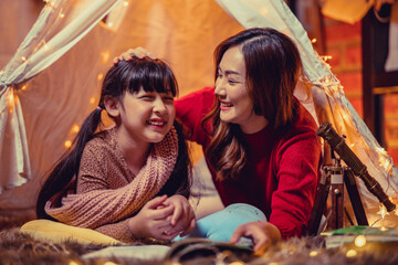 Happy mother and daughters reading a story book together in kids tent on Christmas eve. Celebrating Xmas at home.