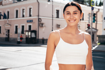 Fototapeta na wymiar Young beautiful smiling hipster woman in trendy summer white top and shorts clothes. Sexy carefree model posing in the street at sunny day. Positive brunette female. Cheerful and happy