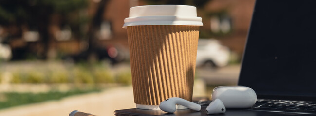 Take away coffee in craft recycling paper cup with paper notebook laptop with wireless headphones. Mockup Coffee break. Audio healing, sound therapy wellness rituals, positive mental health habits