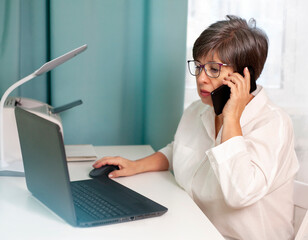 woman sitting at a desk with a laptop and talking on the phone