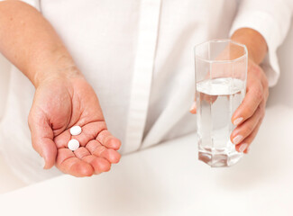 hand with pills and glass of water on white table