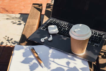Take away coffee in craft recycling paper cup with paper notebook laptop with wireless headphones. Mockup Coffee break. Audio healing, sound therapy wellness rituals, positive mental health habits