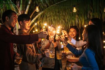 Portrait of Happy Asian group of friends having fun with sparklers outdoor - Young people having fun with fireworks at night time - People, food, drink lifestyle, new year celebration concept.