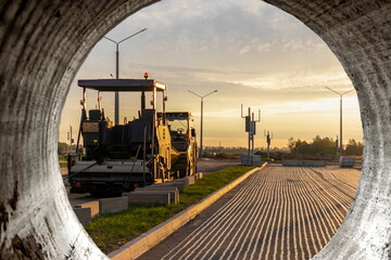 Road repair and asphalt paving with a specialized machine in the evening against the backdrop of...